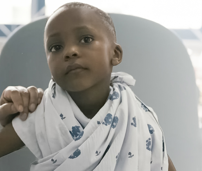 A child in a colorful outfit, smiling and sitting on a hospital bed.